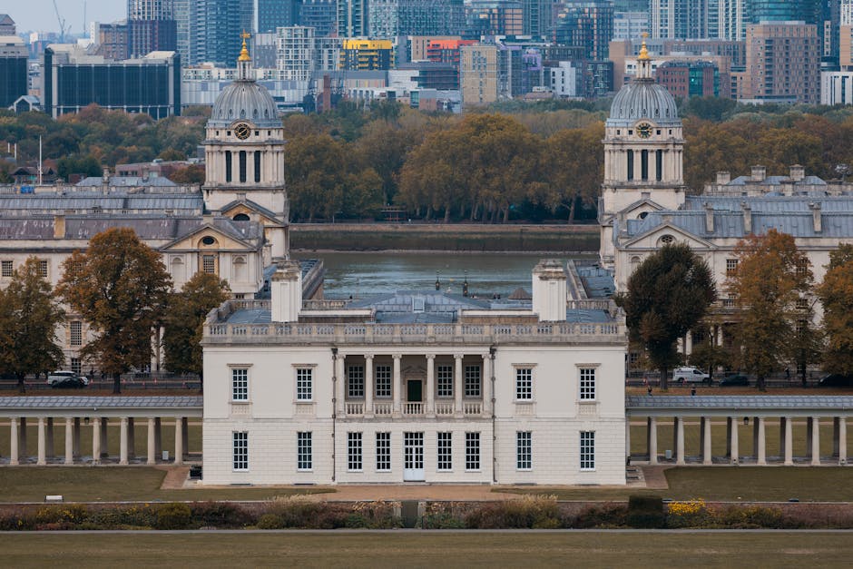 A close-up view of a historic building's exterior wall in daylight, showcasing detailed stonework, decorative columns, and large rectangular windows with metal grills, illuminated by warm sunlight tha